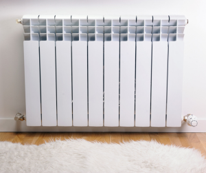 Radiator with white fluffy rug on the floor in front of it.